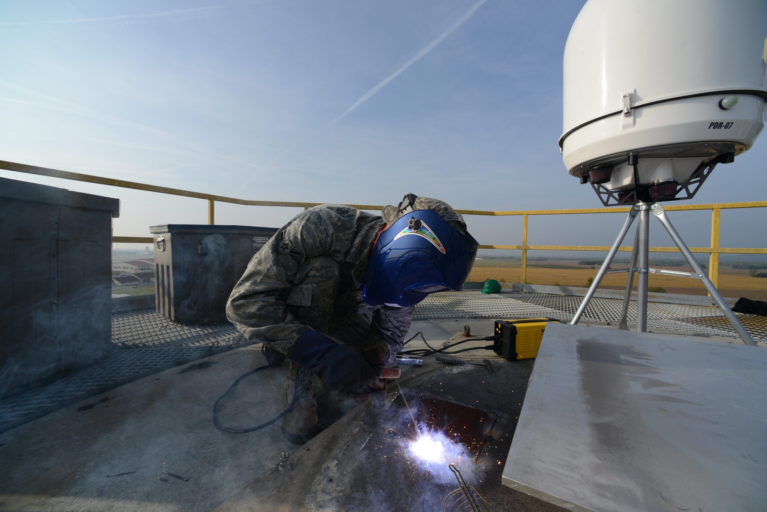 An air force welder working to install a portable radar system from EWR on an elevated platform.