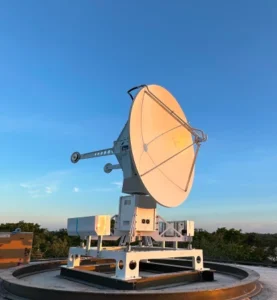 Large parabolic satellite dish mounted on a metal pedestal on a rooftop against a clear blue sky.